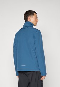 Blue, high-collared jacket with a smooth texture, features a zip closure, long sleeves, and a reflective detail at the bottom hem.