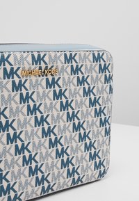 Borsa a tracolla blu e bianca con motivo a raggiera, caratterizzata da una trama intrecciata e con il logo "Michael Kors" in oro. Forma rettangolare, design con chiusura a zip.