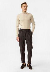 Beige coltrui gecombineerd met hooggetailleerde donker gestreepte broek met dubbele knopen en een geplooide voorkant.