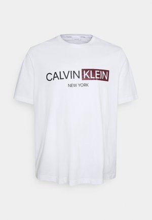 Bílé tričko s krátkým rukávem s nápisem „CALVIN KLEIN“, „KLEIN“ je bílé na vínovém pozadí a pod ním je černě vytištěno „NEW YORK“.