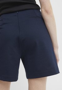 Navyblauwe katoenen shorts met een gladde textuur, een getailleerde pasvorm en een achterknopdetail, eindigend ter hoogte van de bovenbenen.