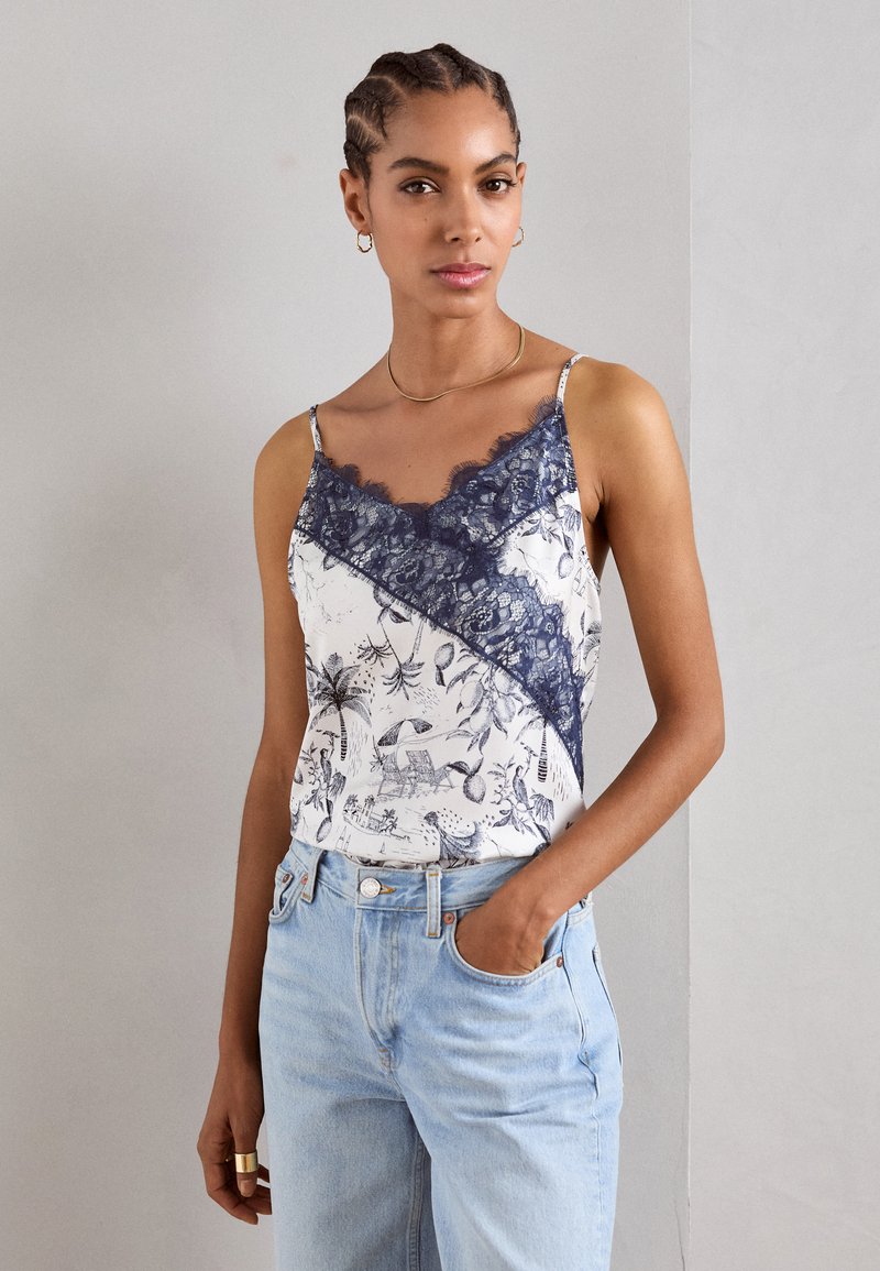 Camisol de satén con encaje en azul marino, presenta un corte geométrico con estampado floral. Usado con jeans de mezclilla azul claro.