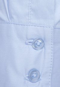 Světlomodrá látka zblízka s dvěma průhlednými plastovými knoflíky a viditelným šitím. Textura je hladká s mírně matným povrchem.
