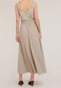 Robe maxi plissée en beige clair avec un dos en V plongeant, des bretelles tressées et une taille élastique pour le confort.