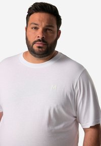 Bílý bavlněný tričko s kulatým výstřihem a krátkými rukávy, s malým vyšívaným logem „M“ v jemném odstínu na hrudi.