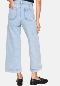 Jeans a gamba larga blu chiaro con vita alta, dotati di due tasche posteriori e dettagli a orlo grezzo, abbinati a mocassini neri.