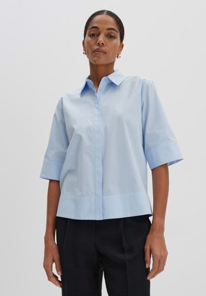 Light blue short-sleeve shirt with a buttoned collar, featuring a straight cut and smooth texture, worn over dark pants.