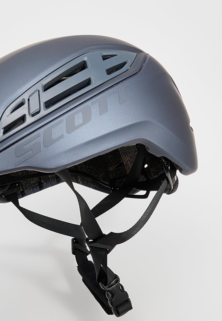 Tmavě modrá cyklistická přilba s ventilačními otvory, nastavitelné popruhy a matným povrchem. Obsahuje vyražené logo na boku.