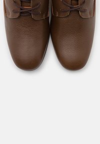 Zapatos de vestir de piel marrón con una textura suave, punteras redondeadas y cordones marrones en contraste, mostrados desde una perspectiva superior.