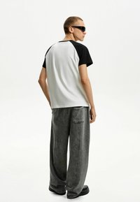 T-shirt color block in bianco e nero con vestibilità rilassata, abbinato a pantaloni larghi grigi con tasca sul retro e texture sbiadita.