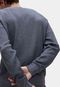 Szary, strukturalny sweter z okrągłym dekoltem i dopasowanymi rękawami. Widok z tyłu pokazuje splot materiału i szczegóły szycia.