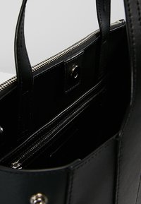 Czarna skórzana torebka na ramię z zamkiem błyskawicznym, wewnętrznymi kieszeniami i srebrnymi akcentami. Gładka tekstura i zorganizowany design z mocnymi uchwytami.