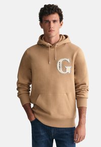 Felpa grigia con cappuccio, tasca frontale, corde di regolazione e logo ricamato "GANT". Tessuto morbido, polsini e orlo a coste. Vestibilità casual.