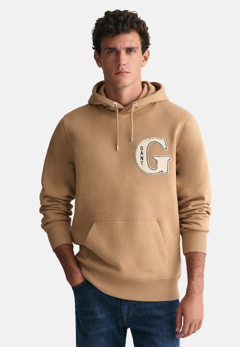 Felpa grigia con cappuccio, tasca frontale, corde di regolazione e logo ricamato "GANT". Tessuto morbido, polsini e orlo a coste. Vestibilità casual.
