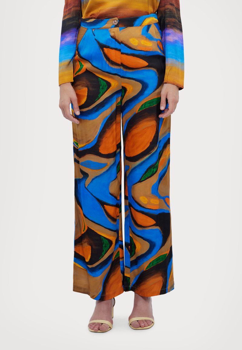 Kolorowe szerokie spodnie wykonane z wzorzystego jedwabiu; mają wiry niebieskiego, pomarańczowego i zielonego koloru na brązowym tle, zakończone zapięciem na guzik.