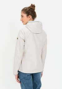 Lys beige vandtæt jakke med hætte, der har en glat tekstur og en subtil glans, parret med blå denimbukser.