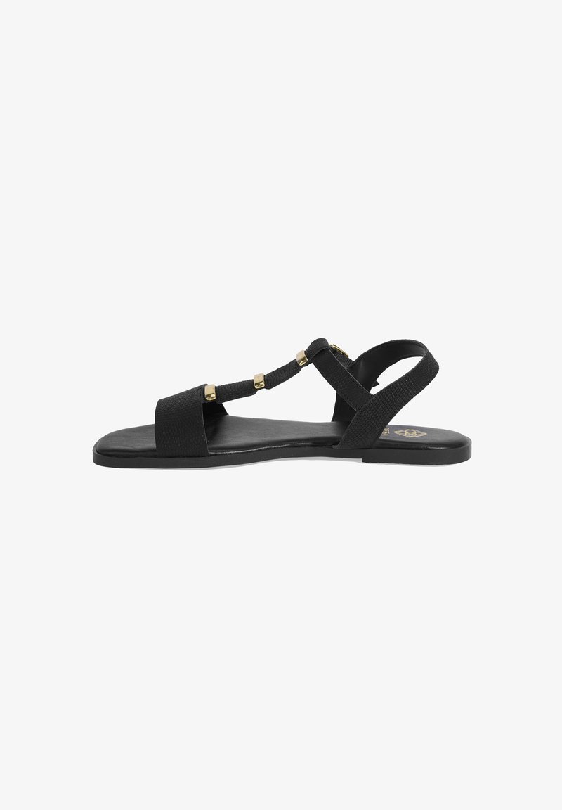 Black flat sandals featuring a textured strap design, gold accents, and a minimalist shape with an open toe. Rubber sole for comfort.
