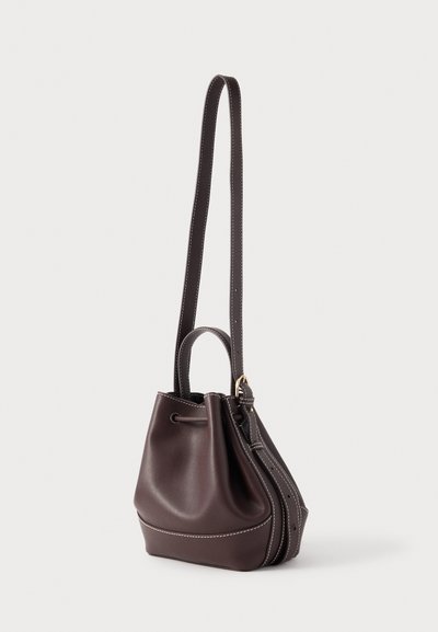Hnedá kožená kabelka v tvare vedra s jedným ramenným remienkom a zvýraznenými švami. Obsahuje sťahovaciu šnúrku a malú hornú rukoväť.