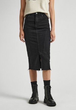 Femme portant une jupe midi en denim noir taille haute avec une fente à l'avant et un ourlet effiloché, associée à des bottes de combat noires à lacets et des chaussettes noires.