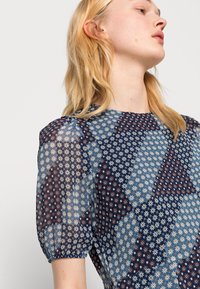 Vestido com padrão floral em tecido transparente, com mangas curtas bufantes, decote redondo e uma palete de cores geométrica em azul e bordô.