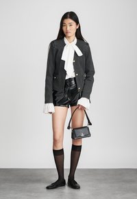 Svart kort jacka med guldknappar, vit blus med en stor rosett, svarta lädershorts, knähöga strumpor och en liten svart handväska.