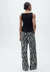 Haut sans manches noir associé à un pantalon large avec un motif zèbre noir et blanc audacieux. Tissu lisse avec un design structuré.