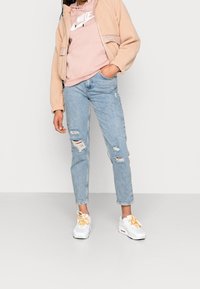 Beige fleece jacket, pink Nike hoodie, light blue distressed jeans, and white sneakers with yellow accents. Visible pockets and frayed hems.