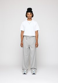 Camiseta blanca de manga corta, pantalones anchos de piernas plisadas en gris, gorro de punto negro, collares de cadena plateados y zapatillas deportivas estampadas.