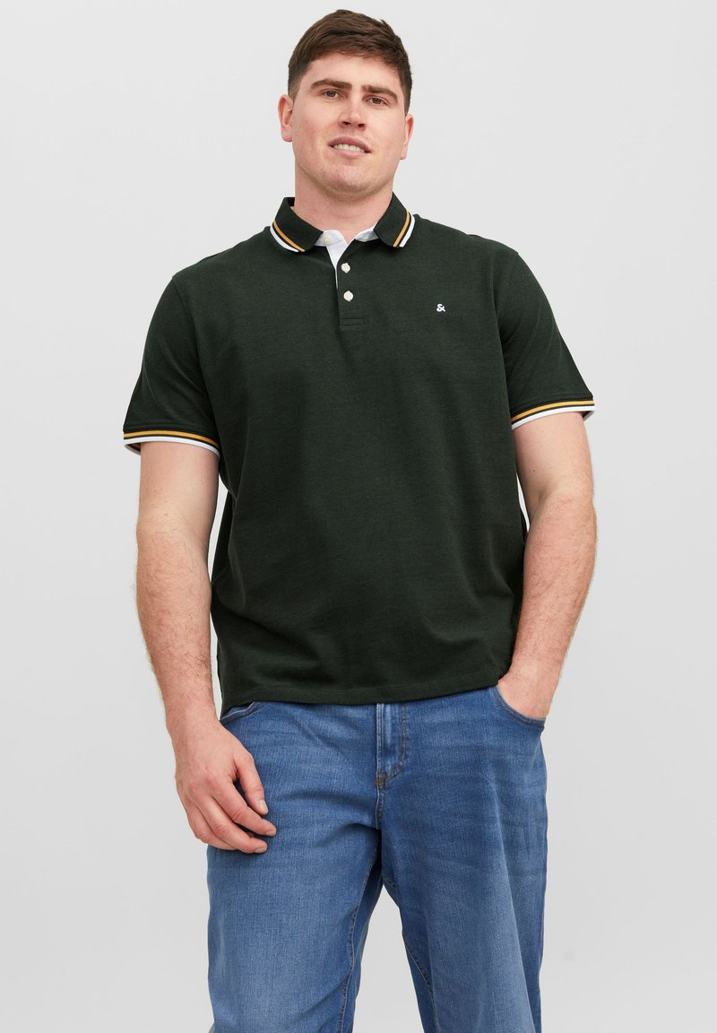 Polo shirt verde scuro con colletto classico, caratterizzato da dettagli a righe bianche e gialle sul colletto e sulle maniche. Tessuto testurizzato.