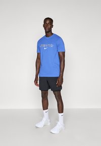 Sininen puuvillapaita, jossa on "JUST DO IT" -grafiikka, yhdistetty mustiin shortsit. Asusteet sisältävät valkoiset Nike-sukat ja kengät. Yksinkertainen muotoilu, rento istuvuus.