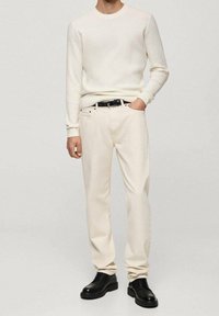 Cream ribbed long-sleeve sweater paired with light beige pants. Finished with a black belt and black leather shoes. Simple, clean lines throughout.