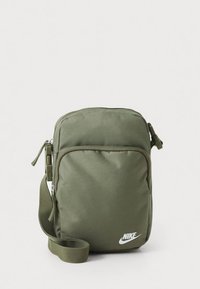 Zelená nylonová crossbody taška se zipovým uzávěrem, obdélníkovým tvarem, nastavitelným popruhem a bílým logem Nike na přední straně.