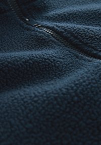 Tamsiai mėlynas fliso švarkas su tekstūruota paviršiaus faktūra, ilgu užtrauktuku ir švelniu audiniu, puikiai tinkantis šilumai ir patogumui.