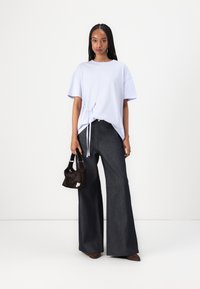 Lys lilla oversized t-skjorte med detalj av knyting i kanten, paret med høyvintede, mørke, vide jeans og en liten svart håndveske.