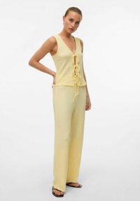 Haut tricot jaune avec un col en V et un détail de nœud à l'avant, associé à un pantalon large assorti. Texture lisse, design décontracté, sans motifs visibles.