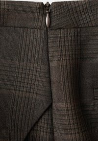 Tessuto a quadri marrone con sottili linee verticali e orizzontali, presenta una cerniera metallica nella parte superiore. Texture liscia con design strutturato.