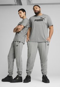 Grå træningssæt bestående af T-shirts med korte ærmer og sweatpants, med sorte Puma-logo detaljer og slanke sorte sneakers.