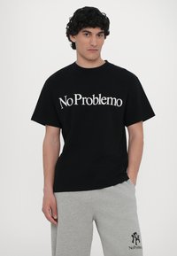 Svart bomull t-skjorte med "No Problemo" trykt i hvitt. Korte ermer, rund hals, avslappet passform. Kombinert med lysegrå joggebukser med logo.