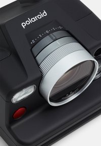 Polaroid camera with a matte black body. Features a round silver lens, a red shutter button, and a textured grip. Modern and compact design.