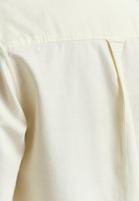 Light yellow striped shirt featuring a straight cut and a back pleat detail. Soft texture with a smooth finish.
