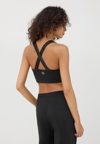 Reggiseno sportivo nero con spalline incrociate sul retro, realizzato in tessuto morbido. Presenta un dettaglio logo sulla parte sottostante del retro.