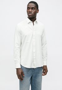 Weißes langärmeliges Hemd mit leichten vertikalen Streifen, knöpfbarem Kragen und abgerundetem Saum, kombiniert mit hellblauen Jeans.