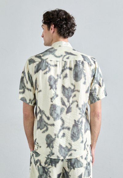 Short-sleeve shirt in light cream with gray marbled pattern, featuring a soft texture and a straight hem. Worn with matching shorts.