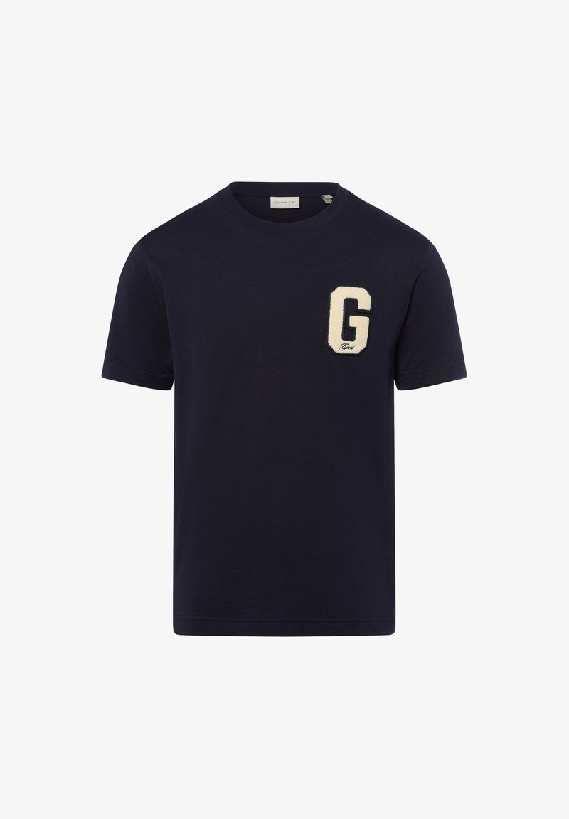 Μπλε βαμβακερό t-shirt με μεγάλο κρεμ «Γ» πα patch στο αριστερό στήθος, κοντά μανίκια και στρογγυλή λαιμόκοψη. Απλός και μοντέρνος σχεδιασμός.