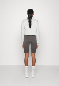 Jasnoszara, oversize bluza, szare szorty rowerowe i białe sneakersy w połączeniu z paskowanymi skarpetkami. Gładki materiał, luźny krój, minimalistyczny design.