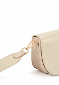 Beżowa skórzana torebka crossbody o gładkiej fakturze, zaokrąglonych krawędziach i złotych akcentach. Posiada regulowany pasek z zaczepem.