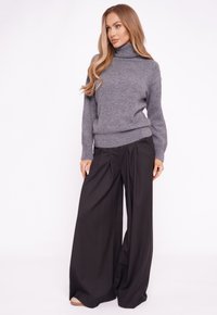 Szary sweter z golfem z prążkowanym dołem, zestawiony z czarnymi szerokimi spodniami z plisami. Gładka faktura tkaniny, minimalistyczny design.