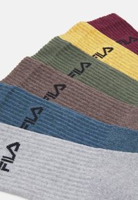 Meias caneladas em cinco cores: cinza, azul, castanho, verde e amarelo, cada uma apresentando o logótipo da Fila em preto. Tecido texturizado.
