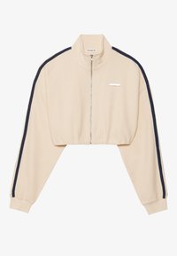 Chaqueta beige recortada con cierre frontal de cremallera, con franjas laterales azul marino y textura acanalada. Incluye una etiqueta sutil de la marca en el pecho.