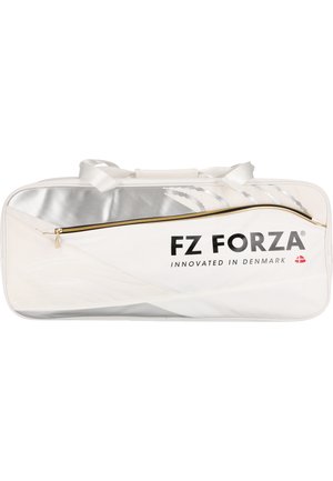 Kvinde i blåt sportstøj står med en stor hvid FZ Forza sportstaske over skulderen og kigger til siden mod en ensfarvet baggrund.